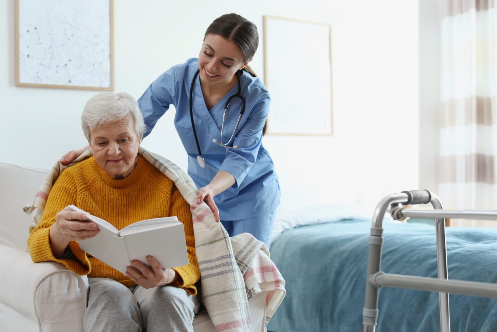A carer placing a blanket around an older woman reading a book